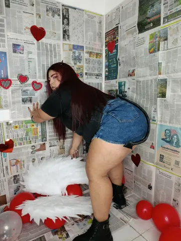 Curvy woman in denim shorts and black t-shirt posing against a newspaper wall background with red balloons.