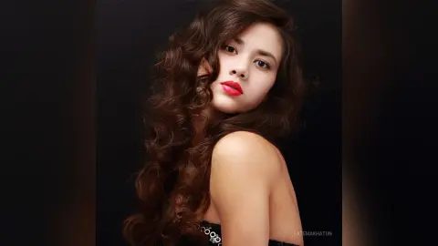 Elegant woman with wavy brown hair and red lipstick posing against a dark studio background.
