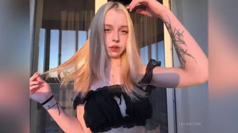 Blonde woman in a black ruffled crop top posing outdoors during golden hour sunset.
