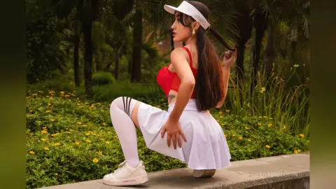 Young woman in red top and white skirt posing in a lush green garden setting.