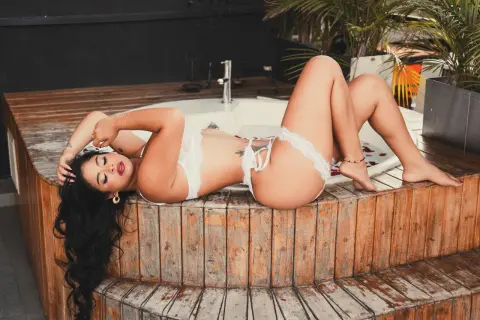 Relaxed woman in white lace lingerie lounging on a wooden deck by a luxury outdoor hot tub.