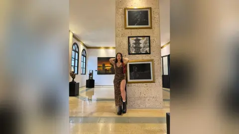 Stylish woman in a leopard print maxi dress posing in a modern art gallery with framed paintings.