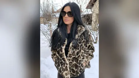 Stylish woman in a leopard print faux fur coat and sunglasses standing in a snowy winter landscape.