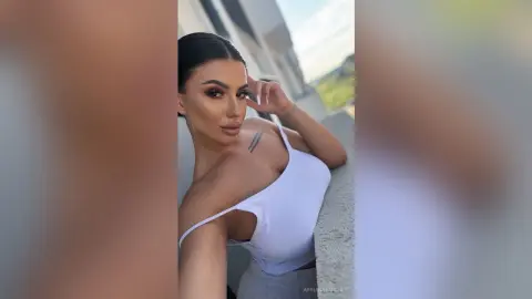 Glamorous woman in a white tank top posing confidently on a sunny balcony with a soft aesthetic mood.