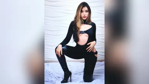JessieLiu poses in a black cutout bodysuit and thigh-high boots against a white textured wall.