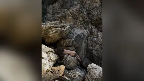 Nude woman relaxing amidst rugged, sunlit rock formations in a serene natural canyon setting.