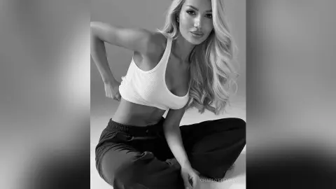 Blonde woman in white ribbed crop top and dark joggers posing in a minimalist studio setting.