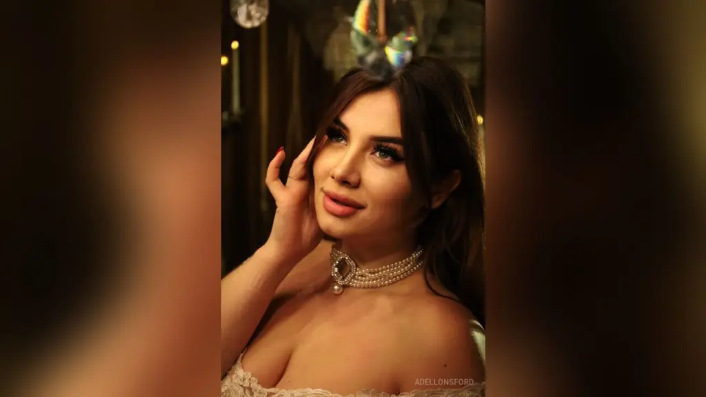 AdelLonsford — AdelLonsford poses in a white lace top and pearl choker while looking toward the camera.
