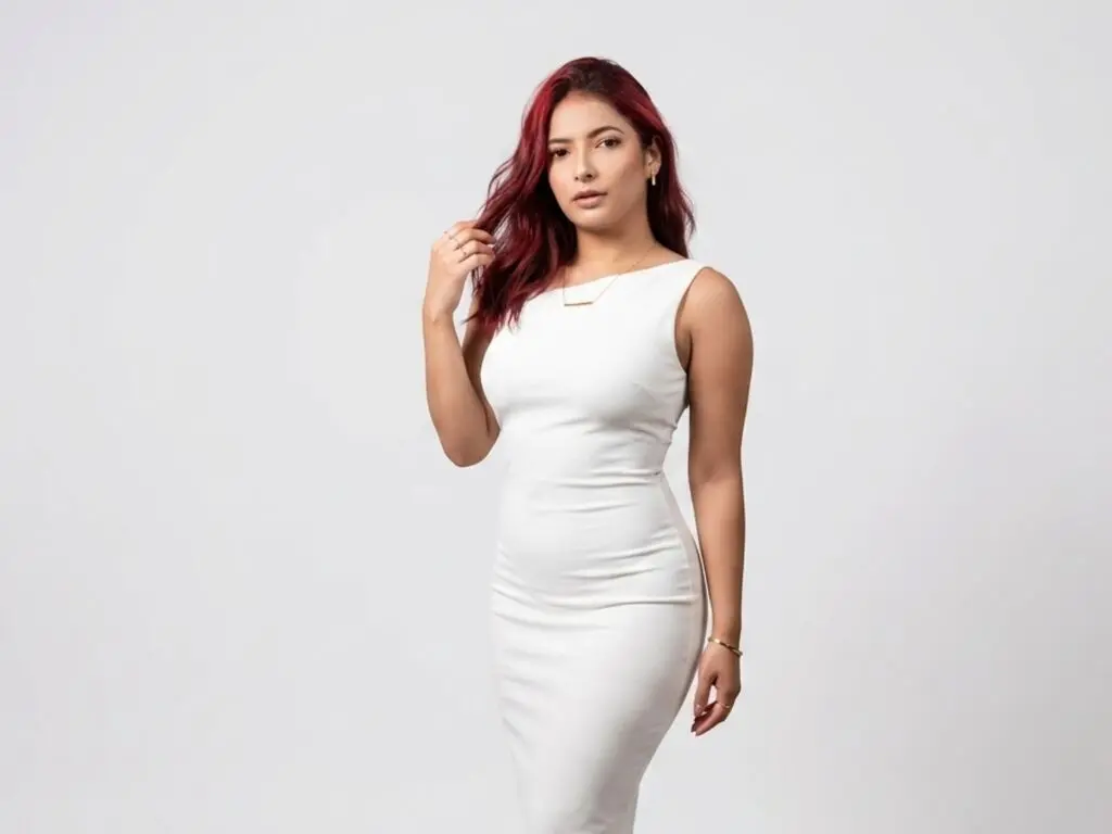 Elegant woman with red hair in a sleek white midi dress posing against a minimalist white background.