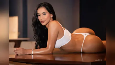 Alison poses naked or in white thong underwear, lying face down on a dark wooden table with her back arched and hair flowing down.