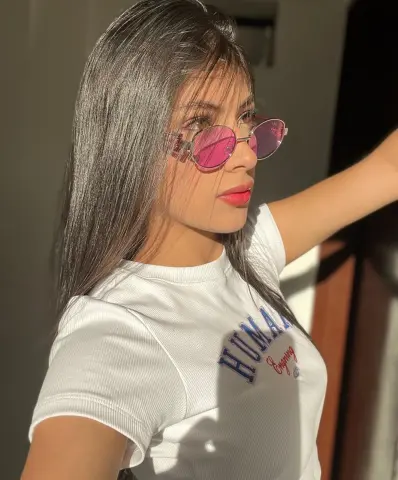 Young woman with long hair wearing pink sunglasses and a white graphic t-shirt in bright sunlight.
