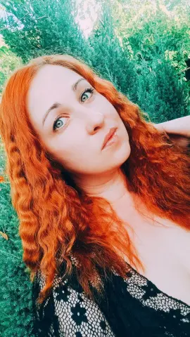 Jill_Stevens poses outdoors with her long, wavy red hair, wearing a black lace top with a star pattern.