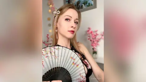 Elegant woman in a black dress holding a floral folding fan in a soft, romantic indoor setting.
