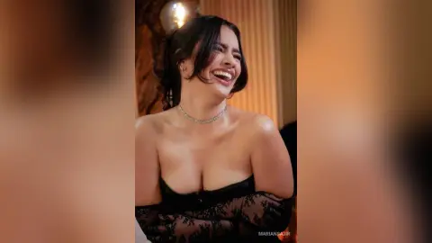Smiling woman in a black lace strapless dress laughing in a warm, dimly lit indoor setting.