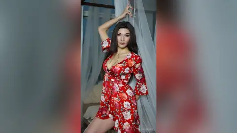 Elegant woman in a red floral midi dress posing by a window in a bright, airy room.