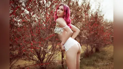 Pink-haired woman in white lace lingerie posing in a dreamy outdoor garden setting.