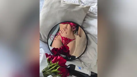 Woman in red lace lingerie relaxing on a bed next to red roses for a romantic mood.
