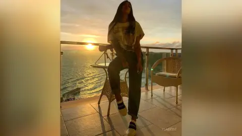 Woman in casual t-shirt and jeans relaxing on a balcony overlooking the ocean at sunset.
