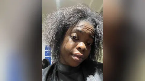 Close-up portrait of a woman with voluminous natural afro hair in a casual indoor setting.