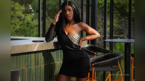 CrischelNovaks poses against a bar wearing a black off-the-shoulder dress with a silver metallic bustier detail.