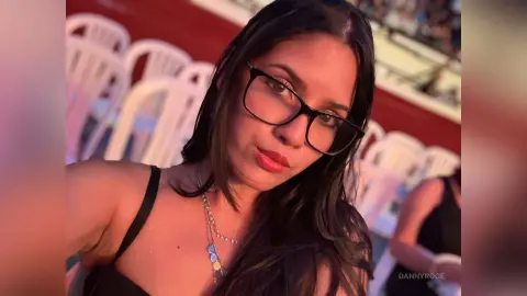 Young woman with long dark hair wearing a black strap top and glasses in a warm, sunset outdoor setting.