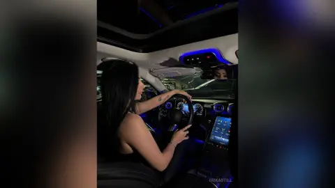Woman with long dark hair sitting in a luxury car interior with blue ambient lighting at night.