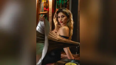 Glamorous woman in a black dress holding a silver umbrella in a moody, dimly lit indoor setting.