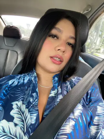 Young woman in a blue tropical print blouse sitting in a car seat wearing a seatbelt.