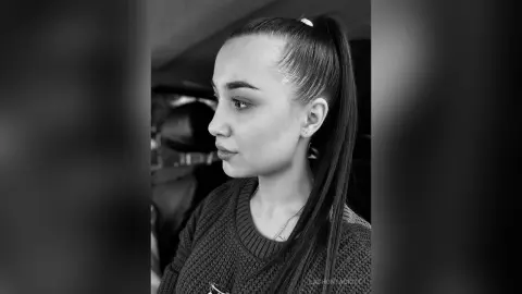 Black and white portrait of a young woman with a high ponytail wearing a cozy knit sweater in a moody setting.