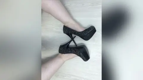 Close-up of a person wearing elegant black sparkly high heel platform pumps on a light wood floor.