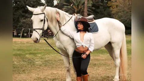 FlorenciaCopper stands next to a white horse wearing a white button-down shirt and black leggings.