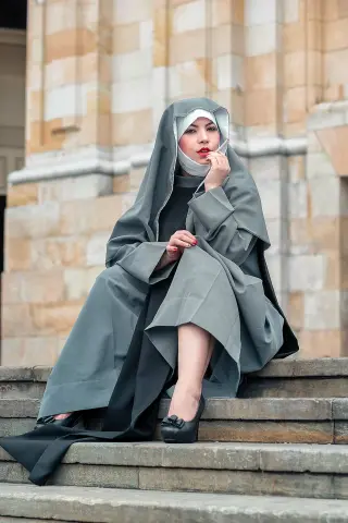 Elegant woman in a grey hijab and black gown sitting on stone stairs with a serene expression.