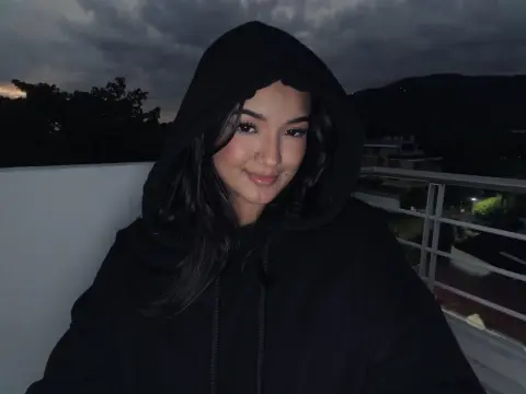 Smiling young woman in a black oversized hoodie relaxing on a balcony at dusk.