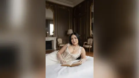 Elegant woman in a white lace dress reading a book in a luxurious vintage bedroom.