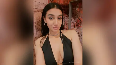 Young woman in a black halter neck top posing in a warm, dimly lit indoor setting.