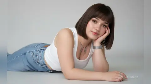 Young woman with short brown hair in a white tank top and blue jeans lying on a white floor.