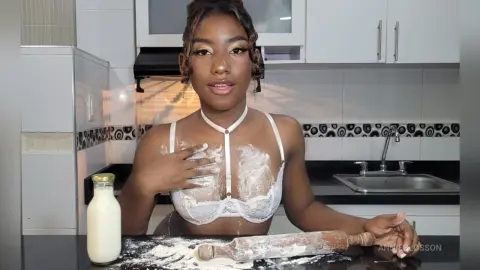 Young Black woman in white lace lingerie baking with flour in a modern kitchen setting.