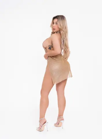 Glamorous blonde woman in a shimmering gold mini dress and silver heels posing against a white background.