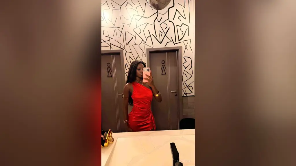 Black woman in a pink bikini and blue headwrap taking a confident mirror selfie in a modern bathroom.