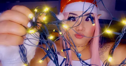 Woman with pink hair and Santa hat holding glowing fairy lights in a cozy festive mood.