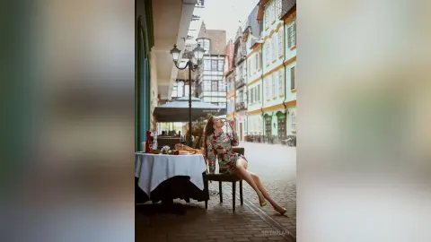 Stylish woman in a floral dress enjoying a meal at an outdoor cafe in a charming European cobblestone street.