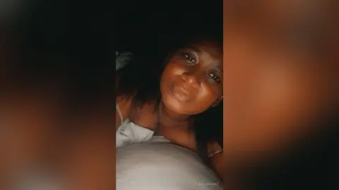 Young woman in white loungewear relaxing in a dimly lit bedroom with a cozy, peaceful mood.