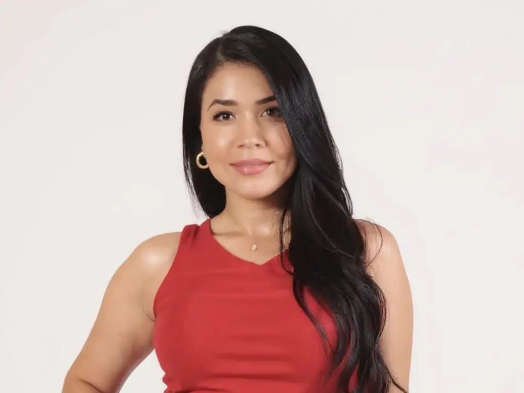 Smiling woman with long dark hair wearing a red sleeveless top against a plain white background.