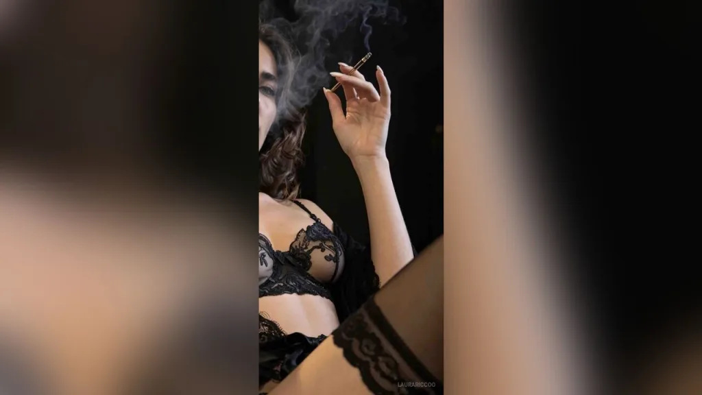 LauraRiccoo — LauraRiccoo wears black lace lingerie while holding a lit cigarette and blowing smoke.