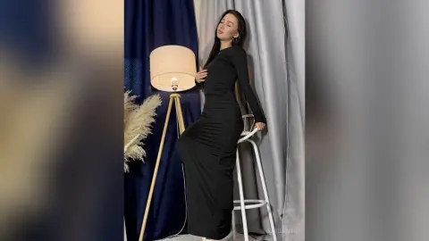 Elegant woman in a long black maxi dress posing gracefully in a studio with soft lighting.
