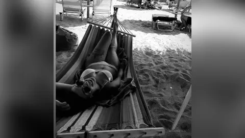 Relaxed woman in bikini relaxing in a striped hammock on a sunny beach.