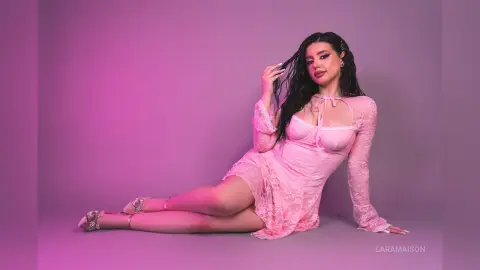 Young woman in a pink lace dress sitting against a purple background in a dreamy, feminine mood.