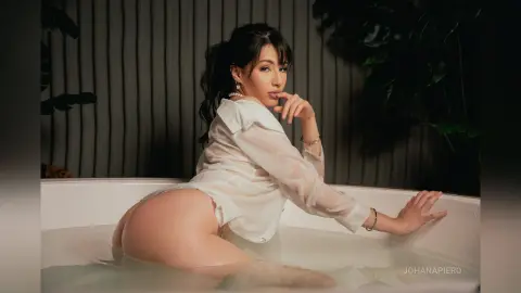 JohanaPiero — Elegant woman in a white silk shirt relaxing in a milky bath against a dark tropical leaf background.