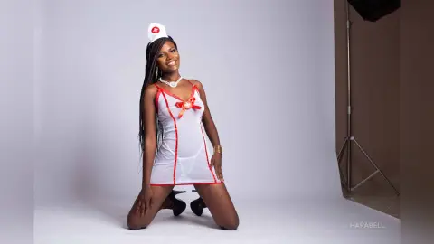 Smiling Black woman in a white and red nurse costume posing in a studio setting.
