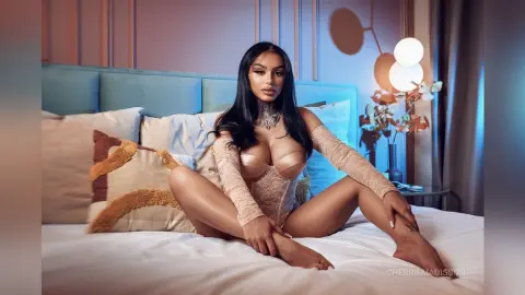 Glamorous woman in lace lingerie sitting on a bed in a cozy, dimly lit bedroom setting.